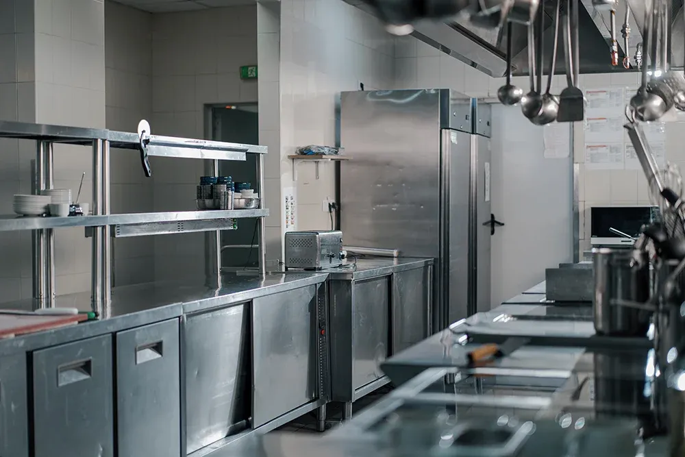 Clean, empty commercial hotel kitchen with stainless steel counters, shelving and hanging utensils after a deep clean