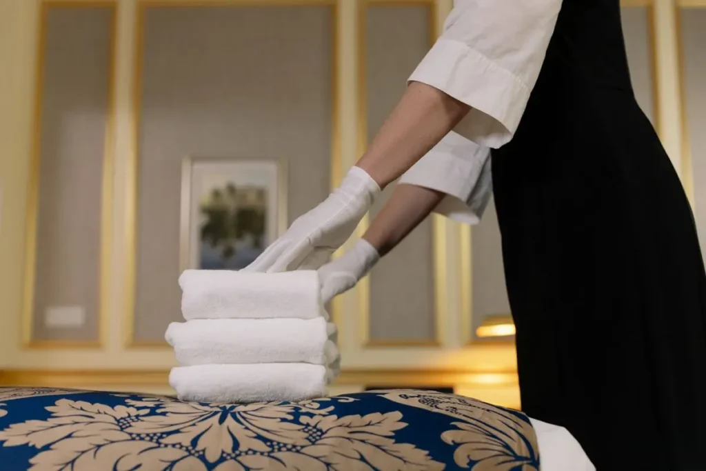 Hotel housekeeper carrying a stack of fresh white towels into a guest room